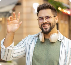 Açık havada, kulaklık takmış ve el sallayan, güler yüzlü bir öğrenci; iletişim ve dil pratiği konusunda kendine güveni simgeliyor