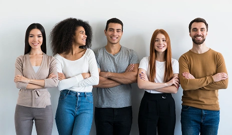 Kollarını kavuşturmuş ve gülümseyen bir grup genç yetişkin öğrenci; bu görüntü, takım çalışmasını ve dil öğrenme topluluğunu simgeliyor